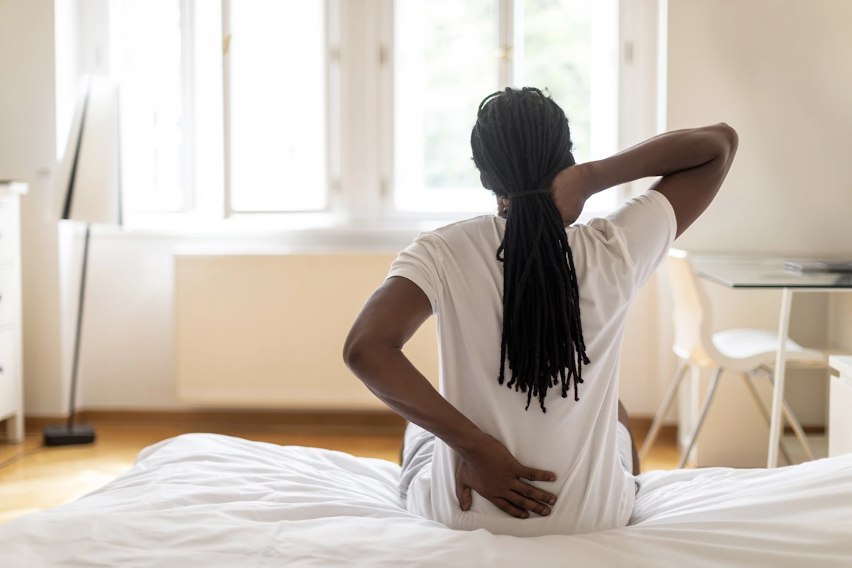Un homme assis sur le lit qui se tient le dos