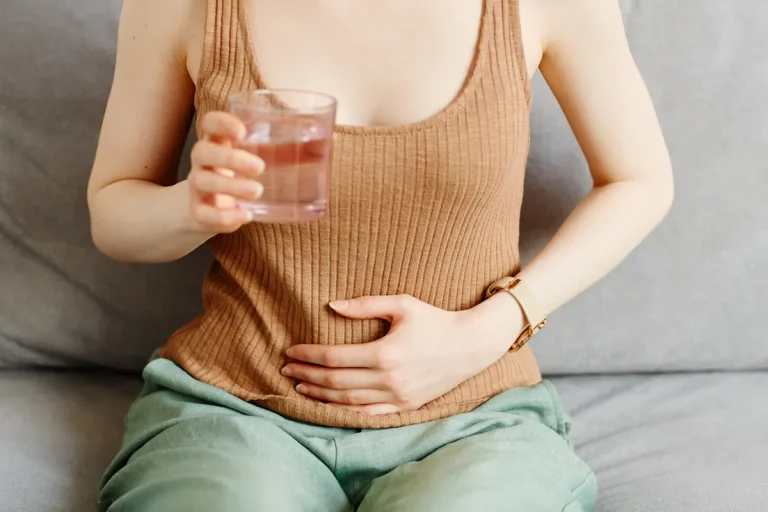 Une femme qui se tient le ventre et un verre d'eau dans l'autre main