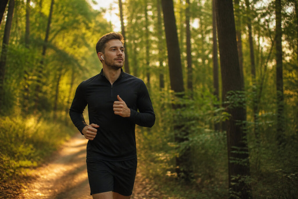 Un jeune homme en tenue de sport court sur un chemin forestier en écoutant de la musique.