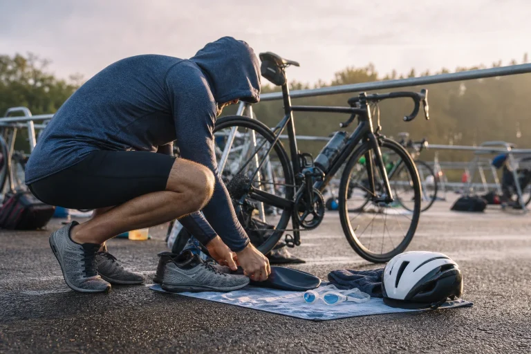 Un triathlète noue ses chaussures près de son vélo, de lunettes de natation et d’un casque.